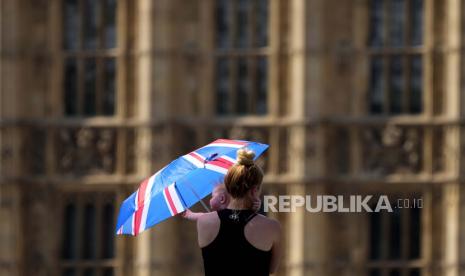 Seorang ibu melindungi bayinya dari matahari dengan payung di Westminster Bridge di London.