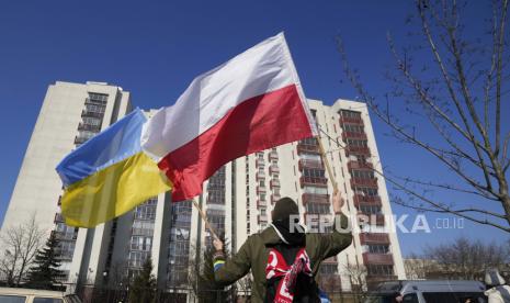 Seorang pria mengibarkan bendera Ukraina dan Polandia selama demonstrasi di depan sebuah gedung yang menampung diplomat Rusia di Warsawa, Polandia, Minggu, 13 Maret 2022. Pemerintah Polandia pada Kamis (19/1/2023) mengkritik seruan pelonggaran sanksi Barat terhadap Rusia dan mengatakan mereka tetap pada sikap tegasnya.