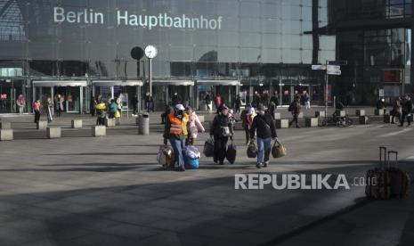  Seorang sukarelawan berbaju merah membantu para pengungsi dari Ukraina setelah mereka tiba di stasiun kereta utama di Berlin, Jerman, Rabu, 16 Maret 2022. Perang Ukraina telah mengubah ruang bawah tanah stasiun kereta api utama kaca dan baja Berlin menjadi sebuah kota pengungsi yang luas di mana pasukan kecil sukarelawan dengan rompi kuning dan oranye menawarkan segalanya mulai dari sampo hingga pengisi daya ponsel hingga pengungsi yang kelelahan. Masuk di latar belakang berbunyi: Stasiun Utama Berlin.