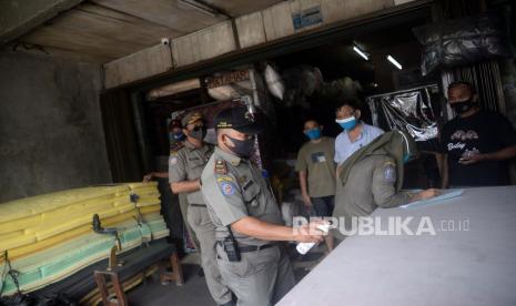 Petugas Satpol PP memeriksa potokol kesehatan saat melakukan pengawasan PSBB di salah satu tempat usaha.