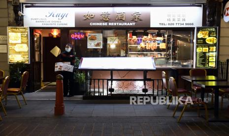 Seorang pegawai dengan menggunakan masker menanti pembeli  di sebauh restoran di Soho, London, Selasa (22/9). Perdana Menteri Inggris Boris Johnson mengumumkan bahwa tempat pub dan restoran akan tutup pada pukul 10 malam hal ini akibat karena lonjakan kasus Covid-19 di seluruh Inggris Raya. AP/Alberto Pezzali