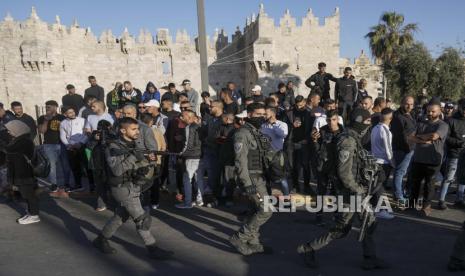 Warga Palestina menyaksikan pasukan keamanan Israel berpatroli di dekat Gerbang Damaskus, tepat di luar Kota Tua Yerusalem, Rabu, 20 April 2022.