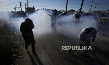 Warga Palestina dan aktivis perdamaian Israel melarikan diri dari gas air mata yang ditembakkan oleh pasukan keamanan Israel, selama demonstrasi menentang pemukiman Yahudi Tepi Barat, dekat kota Salfit, Tepi Barat, Rabu, 27 Juli 2022.