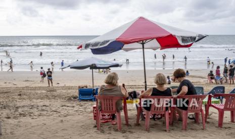 Wisman duduk di pantai Kuta, Bali, Indonesia, 27 Desember 2022. Kantor Imigrasi Bali mencatat sekitar 280.000 wisman datang saat liburan Natal dan Tahun Baru.