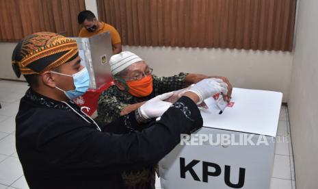 Petugas Kelompok Penyelenggara Pemungutan Suara (KPPS) mengenakan pakaian tradisional Jawa memandu pemilih memasukkan surat suara ke kotak suara saat Pilkada 