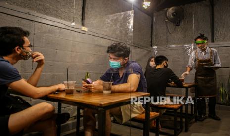 Pengunjung dengan sekat plastik duduk berjaga jarak di sebuah kedai kopi.