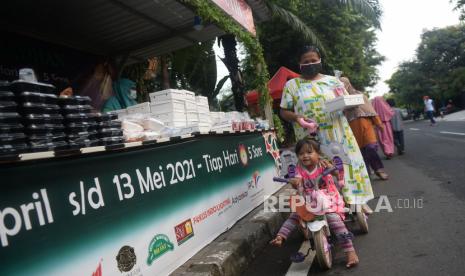 Sejumlah warga mengambil makanan berbuka puasa gratis di Jalan Cempaka Putih Tengah, Jakarta, Ahad (18/4). Sekitar 400-600 paket takjil yang disajikan mulai dari kue, kolak, gorengan, mie ayam, nasi kotak, serta es buah dibagikan secara gratis setiap harinya pada pukul 17.00 selama bulan ramadhan dengan menerapkan protokol kesehatan. Prayogi/Republika.