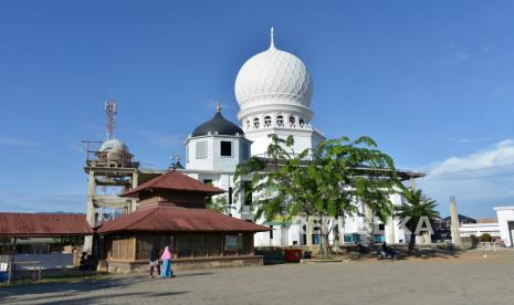 Santri berjalan melintas di depan bangunan lama Masjid Imum Lueng Bata dengan latar belakang proyek pembangunan masjid yang baru di Desa Cot Masjid, Banda Aceh, Aceh, Ahad (25/4/2021). Masjid tua Imum Lueng Bata berkontruksi kayu yang masih terawat itu dibangun oleh Teuku Nyak Raja Imum Lueng Bata pada abad ke-18, seorang tokoh ulama dan juga pejuang dalam melawan penjajahan Belanda. 