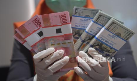 Karyawan menunjukkan uang rupiah dan dolar AS (ilustrasi).