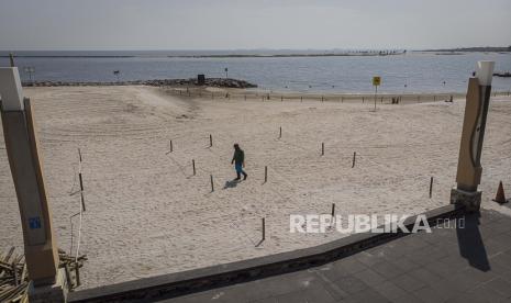 Pekerja berjalan di samping pagar pembatas yang digunakan untuk menjaga jarak pengunjung saat bermain di pantai Lagoon, Taman Impian Jaya Ancol, Jakarta, Rabu (17/6/2020). Pemasangan pagar pembatas tersebut dilakukan untuk mengantisipasi penyebaran COVID-19 jelang pengoperasian kembali Taman Impian Jaya Ancol pada Sabtu (20/6/2020)