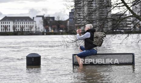 PBB Peringatkan Dunia Hadapi Kenaikan Suhu 2,7 Celsius. Seorang pria berfoto dengan smartphone-nya sambil duduk di bangku di tepi sungai Rhine yang banjir di Cologne, Jerman, Rabu, 3 Februari 2021. Gelombang pasang akibat hujan dan mencairnya salju mengancam pelayaran komersial terbesar di Jerman itu. sungai Rhine.