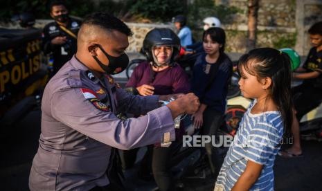 Petugas kepolisian memakaikan masker ke pengendara untuk menekan penularan COVID-19. 