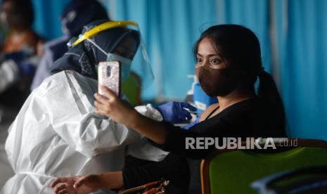 Seorang wanita berfoto saat dokter menyuntikkan dosis vaksin COVID-19 Sinovac selama kampanye vaksinasi massal untuk petugas kesehatan di Jakarta, Indonesia, 15 Februari 2021. Indonesia memulai kampanye vaksinasi COVID-19 nasional pada 14 Januari sebagai negara tercatat lebih dari satu juta kasus, jumlah tertinggi di Asia Tenggara.