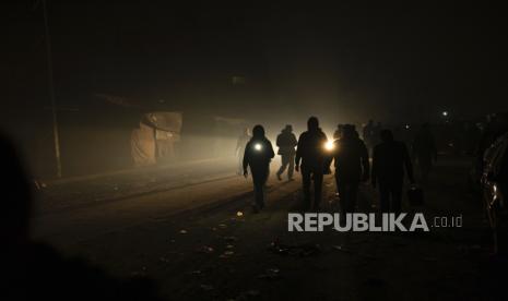 Warga Palestina yang mengungsi akibat pemboman Israel di Jalur Gaza berjalan dalam kegelapan dengan senter di kamp tenda darurat di daerah Muwasi pada Ahad (31/12/2023). 