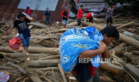 Orang membawa barang-barang mereka ketika mereka berjalan di atas puing-puing rumah yang hancur setelah banjir bandang di Masamba, Sulawesi Selatan, Indonesia, 15 Juli 2020. Menurut Badan Nasional Penanggulangan Bencana Indonesia (BNPB), setidaknya 15 orang telah terbunuh dan puluhan lainnya dilaporkan hilang setelah banjir parah melanda Sulawesi Selatan pada 14 Juli. 