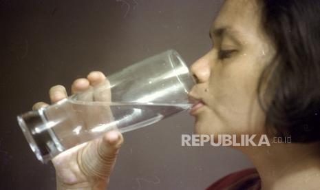 Seorang perempuan sedang minum air putih. Tidak bisa terurai, PFAS ada terus di lingkungan kemudian mengontaminasi air minum, tanah, udara, dan makanan yang dikonsumsi oleh manusia.