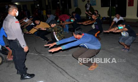 Anggota Polres Gowa memberikan hukuman olah raga fisik kepada  warga yang melanggar pemberlakuan jam malam di Kabupaten Gowa, Sulawesi Selatan, Kamis (7/5/2020) dini hari. Dalam patroli jam malam pada penerapan Pembatasan Sosial Berskala Besar (PSBB) di Kabupaten Gowa tersebut masih ditemukan sejumlah warga yang melakukan aktivitas berkumpul pada malam hari