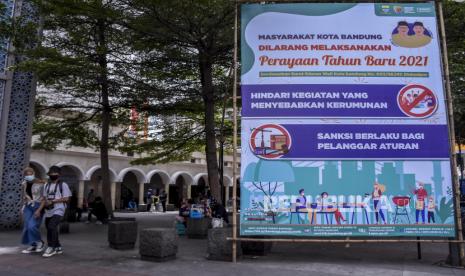 Sejumlah warga melintas di dekat spanduk larangan perayaan tahun baru 2021 di kawasan Alun-Alun Kota Bandung, Jalan Asia Afrika, Kota Bandung, Selasa (29/12). Pemerintah Kota Bandung resmi mengeluarkan surat edaran yang melarang perayaan atau pesta pergantian malam tahun baru. Surat bernomor 003/SE.147-Disbudpar itu ditujukan kepada pimpinan/manajer hotel, pemilik pusat perbelanjaan, kafe, restoran, tempat hiburan, dan seluruh masyarakat Kota Bandung. Foto: Abdan Syakura/Republika