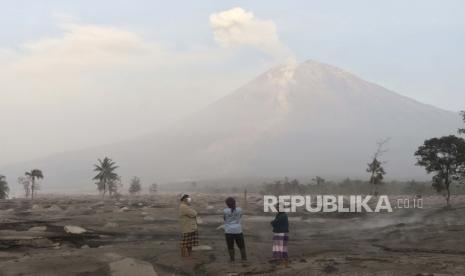 Penduduk desa berdiri di atas area yang tertutup abu vulkanik saat Gunung Semeru menjulang di latar belakang desa Kajar Kuning di Lumajang, Jawa Timur.