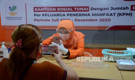 Petugas memotret identitas penerima bantuan sebagai tanda bukti saat Penyaluran Bansos Tunai, di Kantor Pos