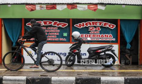 Pesepeda melintas di dekat warung makan yang ditutup dengan tirai di kawasan Cikini, Jakarta