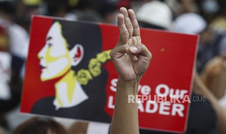  Seorang pengunjuk rasa memberikan hormat tiga jari yang menantang saat yang lain memegang plakat yang menyerukan pembebasan Penasihat Negara Myanmar Aung San Suu Kyi yang ditahan selama protes terhadap kudeta militer, di Yangon, Myanmar, 19 Februari 2021.