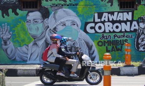 Pengendara motor melintas di depan mural Lawan Corona di Jalan Wonokromo, Surabaya, Jawa Timur, Kamis (26/3/2020). Mural karya Serikat Mural Surabaya tersebut merupakan media edukasi kepada warga agar mencegah potensi penyebaran virus corona atau COVID-19, salah satunya dengan cara memakai masker saat beraktivitas di luar rumah