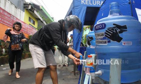 Seorang pengguna jalan mencuci tangannya sebelum masuk di Kelurahan Ketawanggede, Malang, Jawa Timur, Rabu (1/4/2020). Warga di kawasan tersebut secara swadaya melakukan screening kepada para pengguna jalan dengan menyemprotkan disinfektan, mewajibkan cuci tangan, pengukuran suhu tubuh, serta mengurangi akses jalan untuk mencegah penyebaran virus Corona