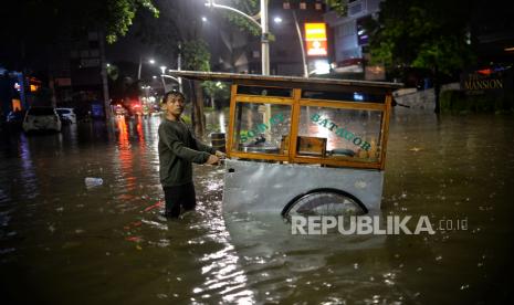 Pedagang mendorong gerobaknya saat menerobos banjir di Jalan Kemang Raya, Jakarta Selatan, Selasa (5/10/2022) malam WIB. 