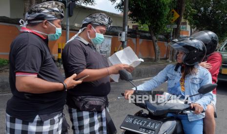 Pecalang atau petugas keamanan adat Bali memeriksa surat keterangan kerja milik warga yang melintas di Tabanan, Bali, Kamis (26/3/2020). Penjagaan dilakukan di setiap perbatasan desa / kota dengan melibatkan unsur pecalang, TNI dan Polri untuk mengurangi lalu lalang orang pascaimbauan gubernur Bali agar masyarakat tetap berada di rumah untuk  mencegah penyebaran COVID-19