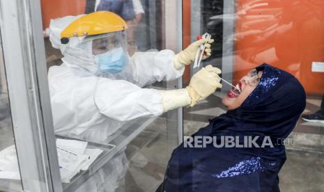  Petugas kesehatan dengan jas hazmat mengumpulkan sampel spesimen melalui plexiglas selama tes usap COVID-19 di Medan, Sumatera Utara, Indonesia, 25 Januari 2021. Indonesia telah mencatat hampir satu juta kasus penyakit coronavirus (COVID-19) sejak awal pandemi.