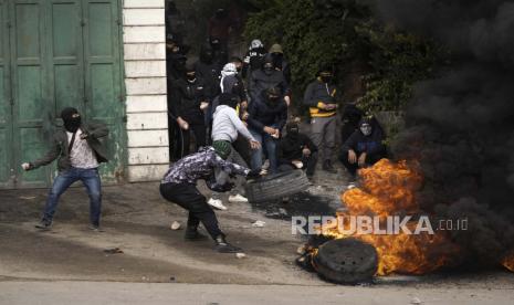 Warga Palestina bertopeng membakar ban saat bentrok dengan pasukan keamanan Israel setelah pemakaman Mufid Khalil di desa Beit Ummar, Tepi Barat, dekat Hebron, Selasa, 29 November 2022. Khalil terbunuh oleh tembakan Israel di Tepi Barat yang diduduki, Palestina Kementerian Kesehatan mengatakan Selasa. Militer Israel mengatakan tentara menembaki warga Palestina yang melemparkan batu dan alat peledak improvisasi dan menembak pasukan.