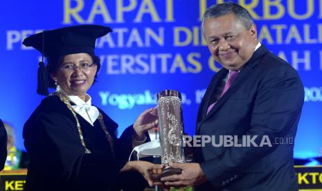 Rektor UGM Ova Emilia (kiri) menyerahkan Anugerah HB IX kepada Gubernur BI Perry Warjiyo saat acara Puncak Dies Natalis ke-73 Universitas Gajah Mada (UGM) di Graha Sabha Pramana, Kabupaten Sleman, Senin (19/12/2022). 