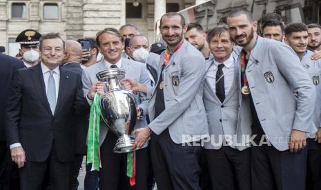 Perdana Menteri Italia Mario Draghi, kiri,  dengan, dari kiri, pelatih Italia Roberto Mancini memegang trofi, kapten Giorgio Chiellini, penyerang Federico Chiesa, staf Gabriele Oriali, dan bek Leonardo Bonucci saat mereka bertemu dengan tim di luar kantor pemerintah Chigi di Roma, Senin, 12 Juli 2021, setibanya mereka di upacara untuk merayakan kemenangan Italia di kejuaraan sepak bola Euro 2020.