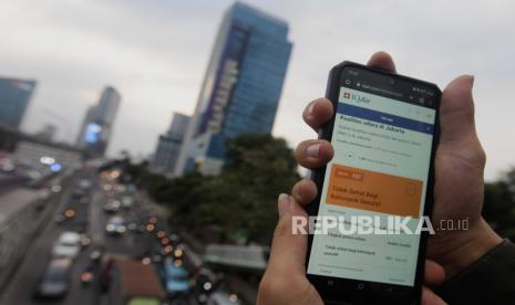 Warga memperlihatkan laman situs IQAir dengan latar belakang kendaraan terjebak kemacetan di Jalan Raya Gatot Subroto, Jakarta. DLH DKI Jakarta mengaku belum bisa menerapkan teknologi modifikasi cuaca