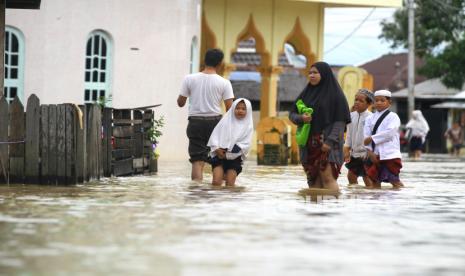 Warga melintasi jalan yang tergenang banjir.