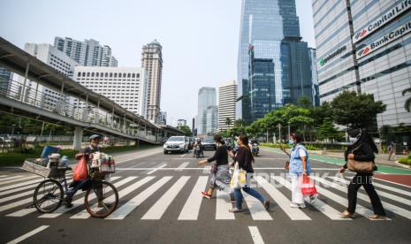 Pekerja dan pedagang kopi keliling menyebrang jalan di Jalan Jenderal Sudirman, Jakarta, Selasa (12/10). Kementerian Tenaga Kerja (Kemnaker) telah melakukan perhitungan besaran Upah Minimum Provinsi (UMP) 2022. 