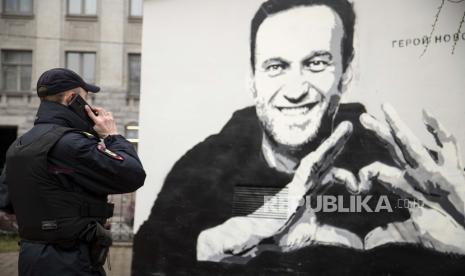 Seorang petugas polisi berbicara di telepon di dekat grafiti pemimpin oposisi Rusia Alexei Navalny yang dipenjara di St.Petersburg, Rusia, Rabu, 28 April 2021. Pihak berwenang Rusia telah menambahkan pemimpin oposisi yang dipenjara Alexei Navalny dan beberapa sekutu utamanya ke daftar teroris dan ekstremis negara itu pada Selasa (25/1/2022).