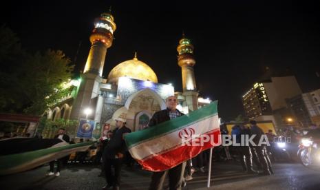 Seorang pria memegang bendera Iran selama unjuk rasa anti-Israel setelah Iran melancarkan serangan pesawat tak berawak terhadap Israel, Ahad (14/4/2024).