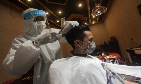 Seorang tukang pangkas rambut menggunakan alat pelindung diri (APD) saat mencukur rambut pelanggannya di Jalan Patih Rumbih, Palangkaraya, Kalimantan Tengah, Jumat (1/5/2020). Menurut pemilik salon, penggunaan APD tersebut sebagai antisipasi terhadap penyebaran COVID-19 serta membuat pelanggan merasa nyaman saat menggunakan jasanya