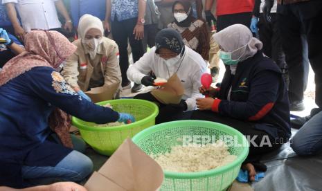 Menteri Sosial Tri Rismaharini (kedua kanan) didampingi Bupati Jember Faida membantu membungkus nasi saat mengunjungi posko banjir Desa Wonoasri di Tempurejo, Kabupaten Jember, Jawa Timur, Senin (18/1/2021). 