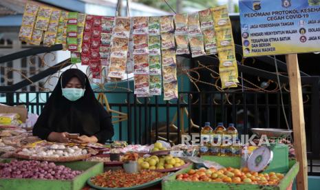 Seorang penjual bumbu masakan mengenakan masker menanti pembeli. Ilustrasi