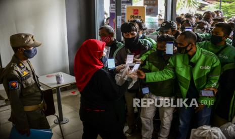 Petugas memberikan pesanan BTS Meal kepada pengendara ojek online di McDonalds Raden Saleh, Cikini, Jakarta, Rabu (9/6). Satpol PP DKI Jakarta menutup sementara McDonalds Raden Saleh  karena terjadinya kerumunan yang mengabaikan protokol kesehatan. Kerumunan tersebut diakibatkan pesanan BTS Meal yang merupakan menu kolaborasi boy band asal Korea BTS dengan McDonalds yang hadir di 50 negara, termasuk Indonesia. Republika/Putra M. Akbar