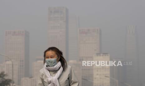  Seorang wanita mengenakan masker wajah untuk melindungi diri dari COVID-19 berjalan di depan gedung perkantoran di Kawasan Pusat Bisnis yang diselimuti kabut polusi di Beijing, Kamis, 18 November 2021. Jika pembatasan dicabut, China diprediksi hadapi gelombang baru Covid-19.