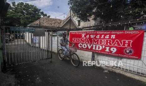 Warga bersepeda di dekat spanduk pemberitahuan zona merah. Ilustrasi