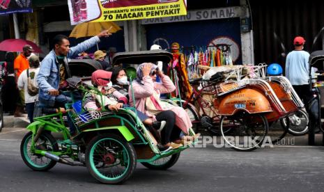 Becak membawa menumpang di dekat parkiran bus pariwisata Jalan Ahmad Dahlan, Yogyakarta, Ahad (5/9). Wisata Yogyakarta mulai menggeliat meski status masih PPKM Level 4. Objek wisata di Yogyakarta hingga saat ini masih di tutup. Namun, puluhan bus pariwisata terpantau memasuki kawasan Malioboro. Hal ini menjadi gairah bagi tukang becak, dan banyak becak menunggu penumpang di dekat area parkir bus pariwisata.