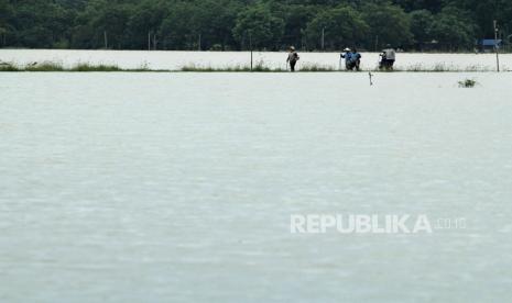 Petani melintasi area sawah yang terendam banjir di Widasari, Kabupaten Indramayu, Jawa Barat, Selasa (5/1/2021). 