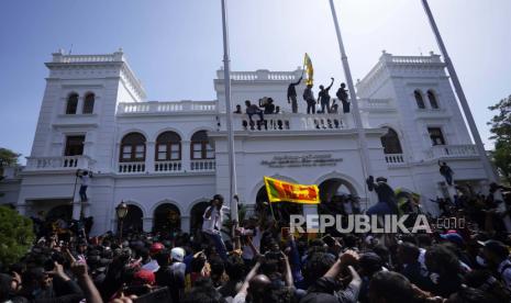  Seorang pengunjuk rasa, membawa bendera nasional, berdiri dengan yang lain di atas gedung kantor Perdana Menteri Sri Lanka Ranil Wickremesinghe, menuntut dia mengundurkan diri setelah presiden Gotabaya Rajapaksa melarikan diri dari negara itu di tengah krisis ekonomi di Kolombo, Sri Lanka, Rabu, 13 Juli 2022. Rajapaksa melarikan diri dengan jet militer pada hari Rabu setelah pengunjuk rasa yang marah merebut rumah dan kantornya, dan menunjuk Perdana Menteri Ranil Wickremesinghe sebagai penjabat presiden saat dia berada di luar negeri. Wickremesinghe dengan cepat mengumumkan keadaan darurat nasional untuk melawan protes yang membengkak atas keruntuhan ekonomi dan politik negara itu.