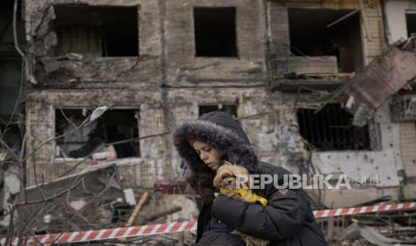 Seorang wanita memegang seekor anjing kecil berjalan di depan sebuah apartemen di sebuah blok yang dihancurkan oleh serangan artileri di Kyiv, Ukraina, Senin, 14 Maret 2022. Menteri Luar Negeri Jean-Yves Le Drian mengatakan Prancis akan mempertimbangkan meminta pertanggungjawaban Rusia pada setiap penggunaan senjata kimia atau bakteriologis dalam invasi ke Ukraina. 