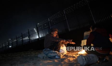 Anggota keluarga Okasha, yang mengungsi dari Jalur Gaza utara, menghangatkan diri di dekat api di luar tenda mereka, dekat perbatasan yang memisahkan Jalur Gaza dan Mesir, di kota Rafah, di Jalur Gaza